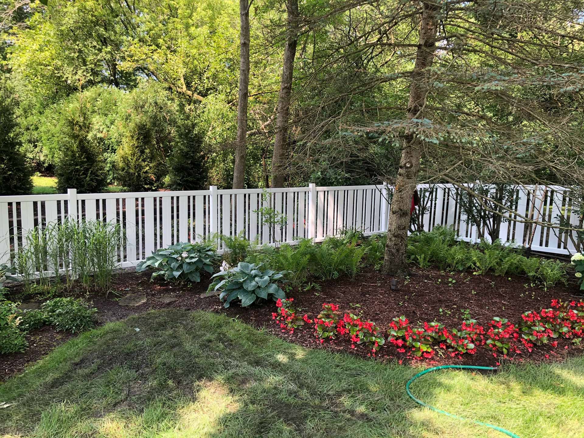 Decorative white vinyl fence installed around a flower bed